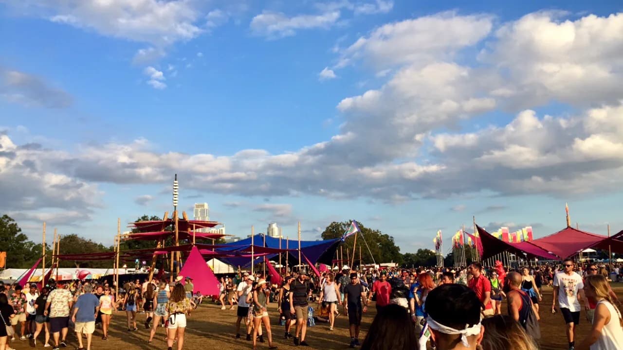 The ACL festival grounds under blue sky with the downtown Austin skyline behind the shade sails