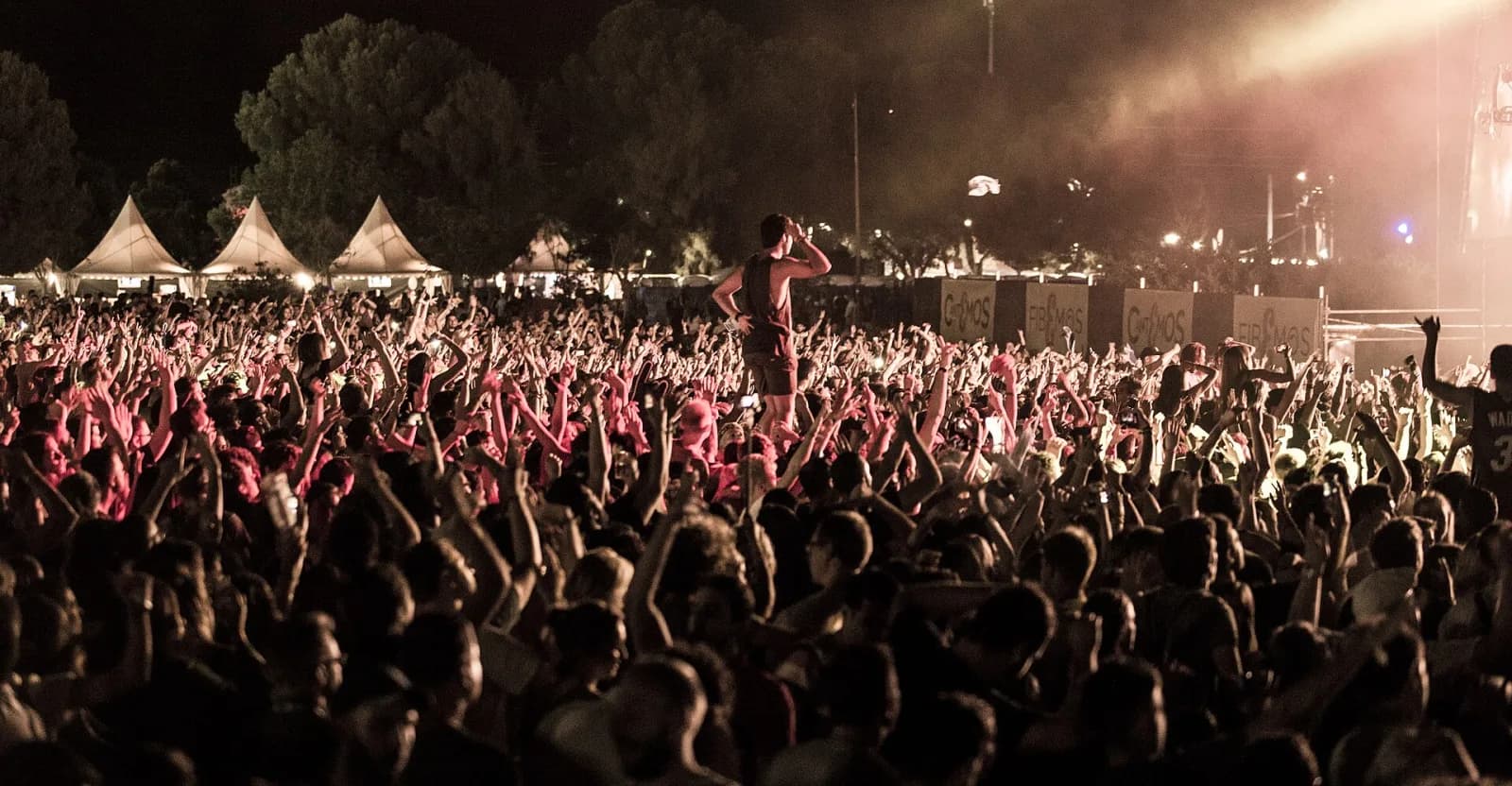A festivalgoer on shoulders above the FIB night crowd, pines and tents behind