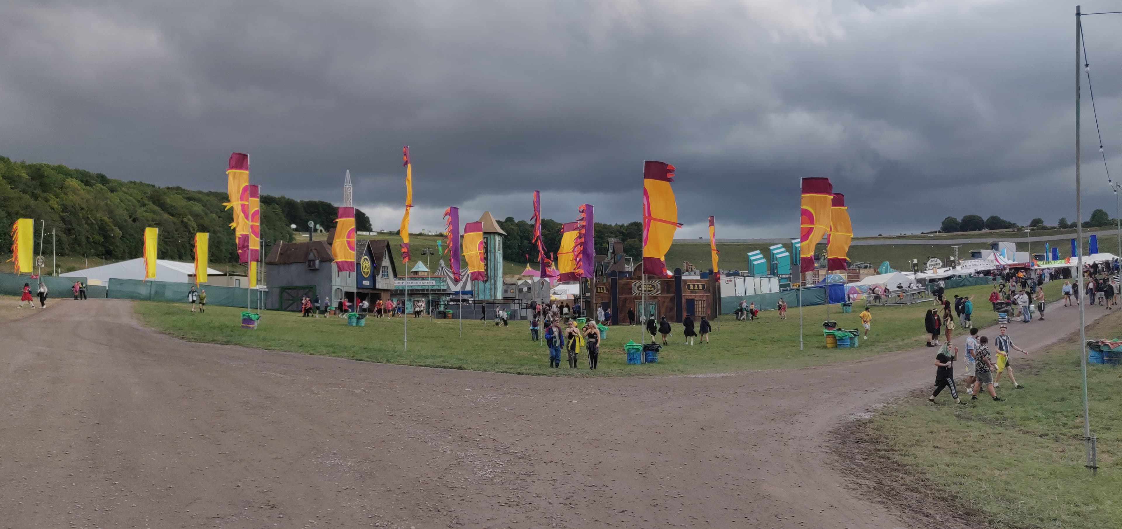 Boomtown Main Drag at Matterley Estate with flags, buildings, hills, and festivalgoers