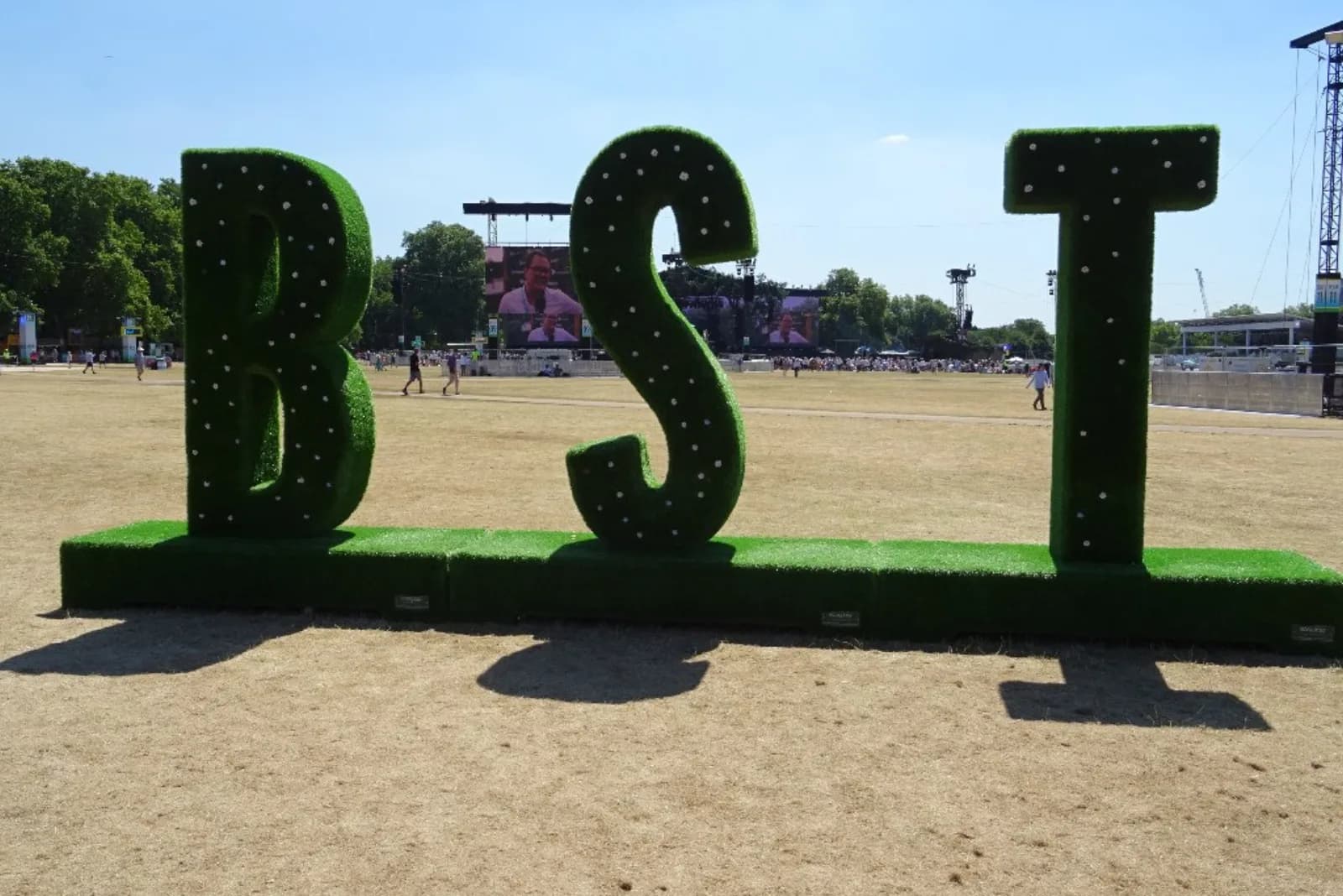 Giant grass-covered BST letters on the Hyde Park festival site with the Great Oak Stage screens behind