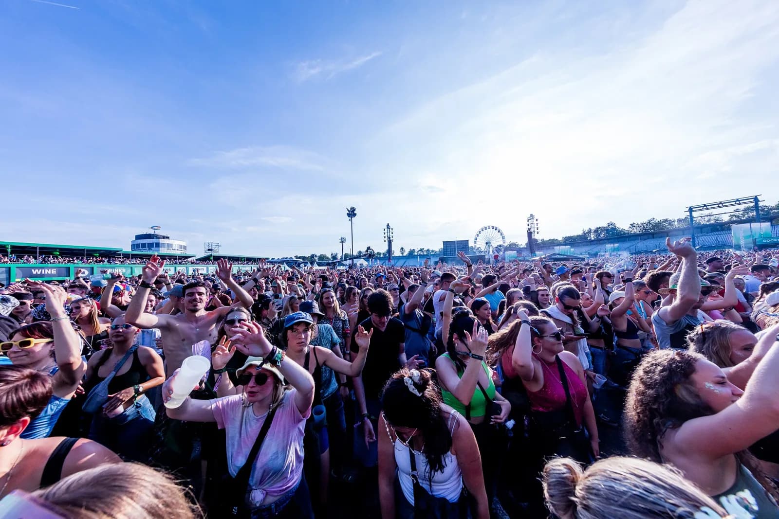 A daytime festival crowd on the Hockenheimring infield with the Ferris wheel and circuit grandstands in the distance