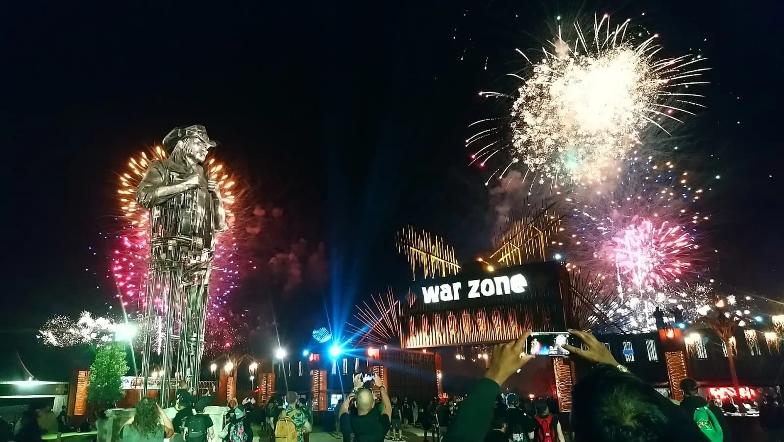 Fireworks over the Hellfest site at night, with the giant Lemmy statue and the War Zone gate lit up