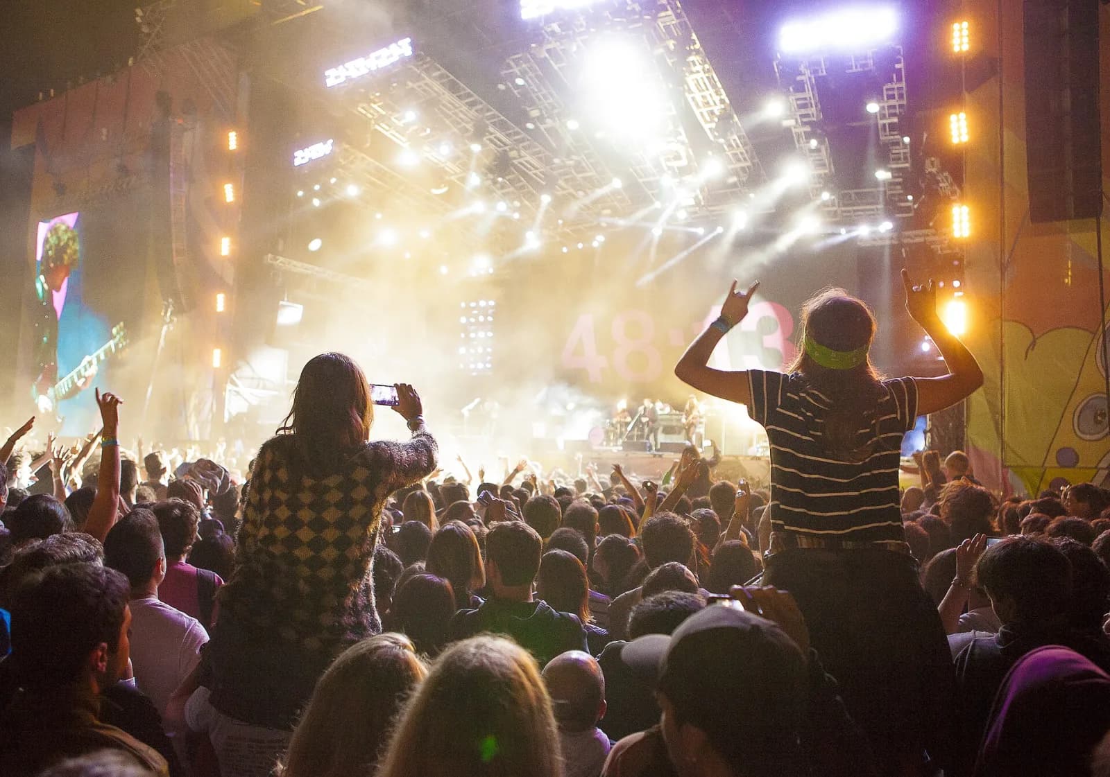 A night-time Lollapalooza Argentina crowd with fans on shoulders silhouetted against a bright main stage