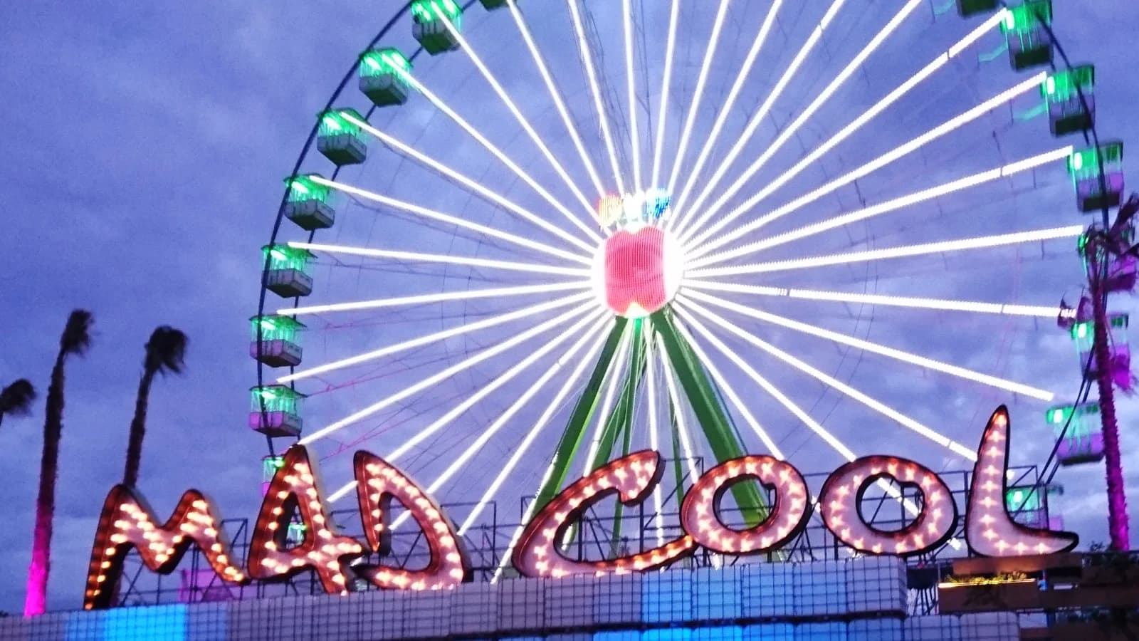 The illuminated Mad Cool sign in front of the ferris wheel at dusk
