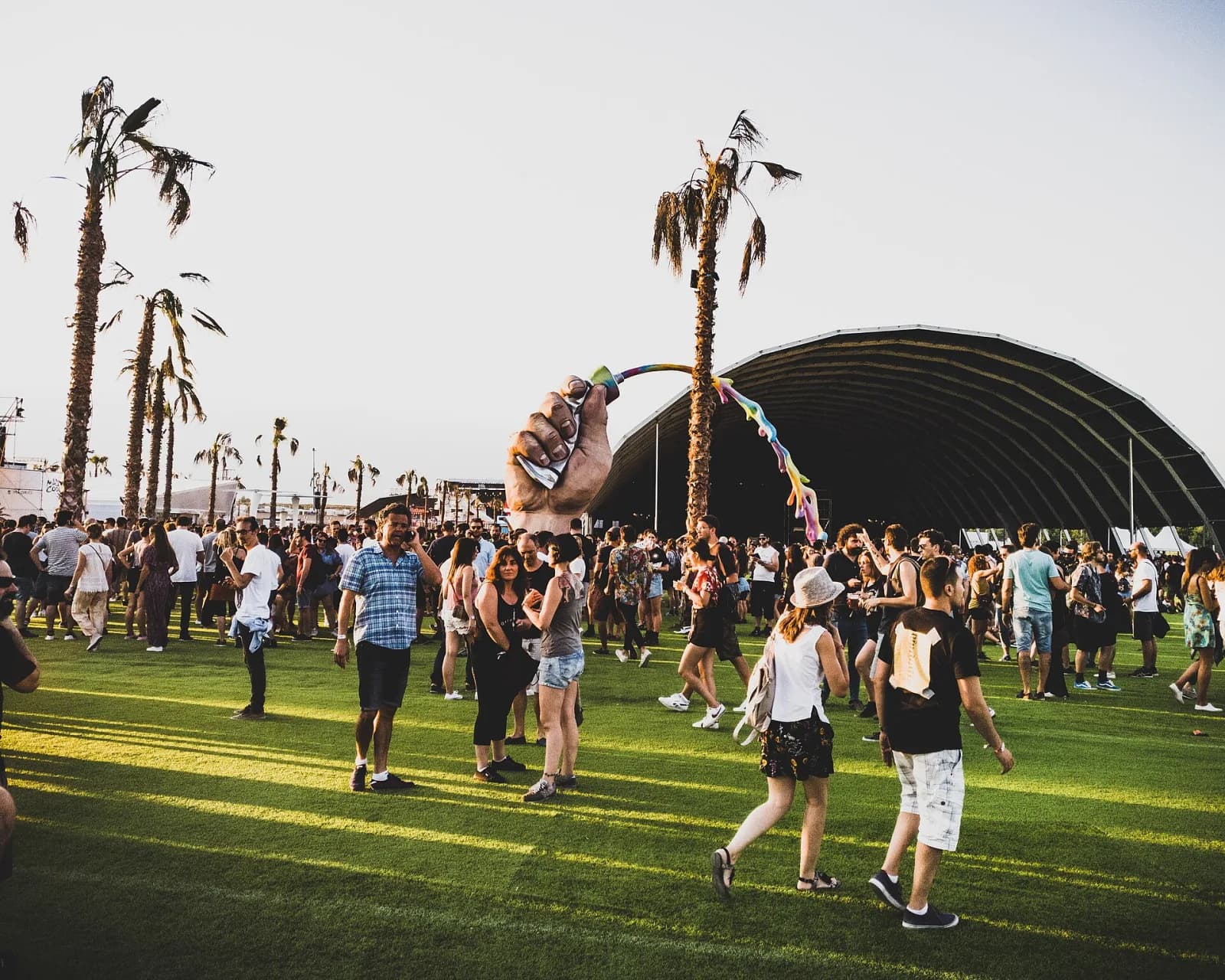 Festivalgoers on green turf between palm trees at the Mad Cool site at golden hour