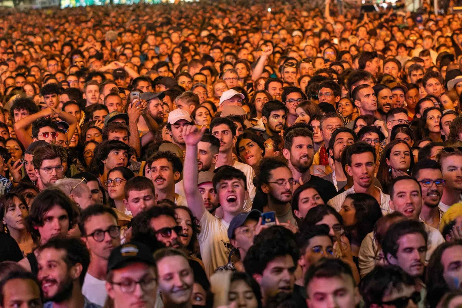 A dense night-time crowd at NOS Alive lit in warm orange light during a headline set