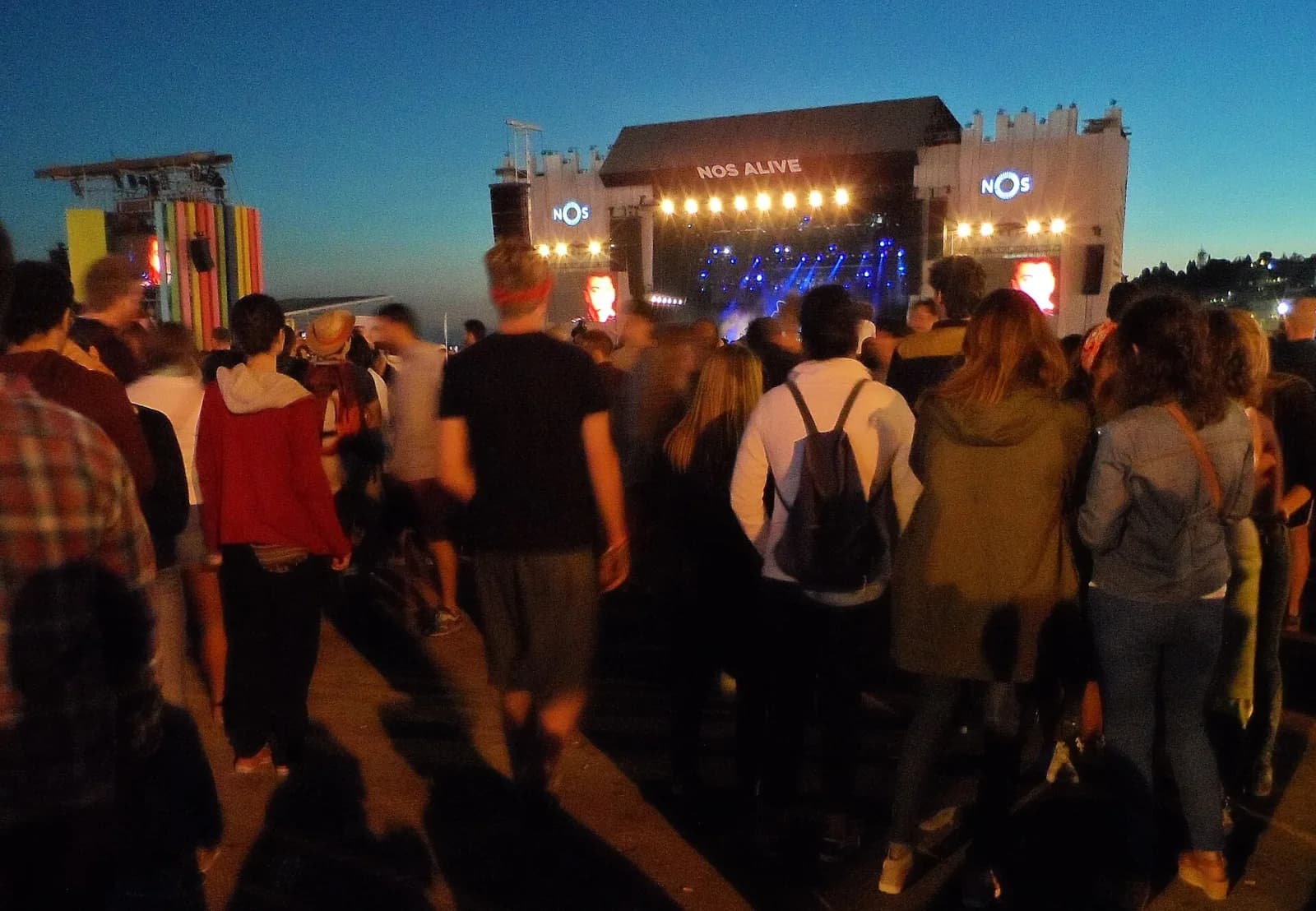 The NOS Alive main stage at dusk with the crowd arriving across the open site