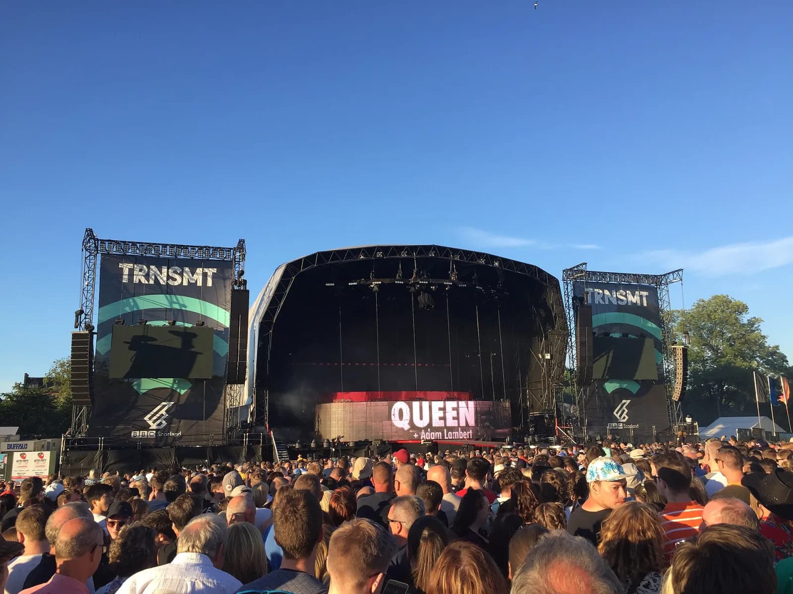 The TRNSMT main stage under a clear blue sky with branded screens either side and the crowd gathering