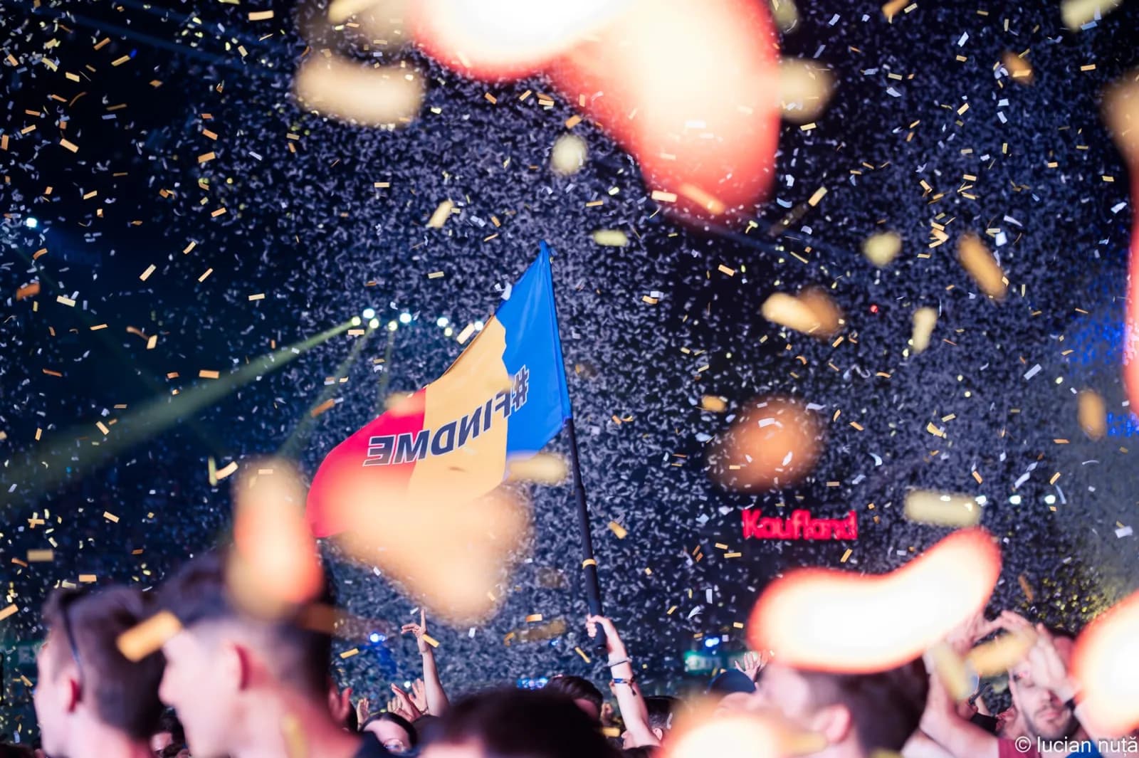 Confetti falling over the UNTOLD crowd at night, with a Romanian flag held up