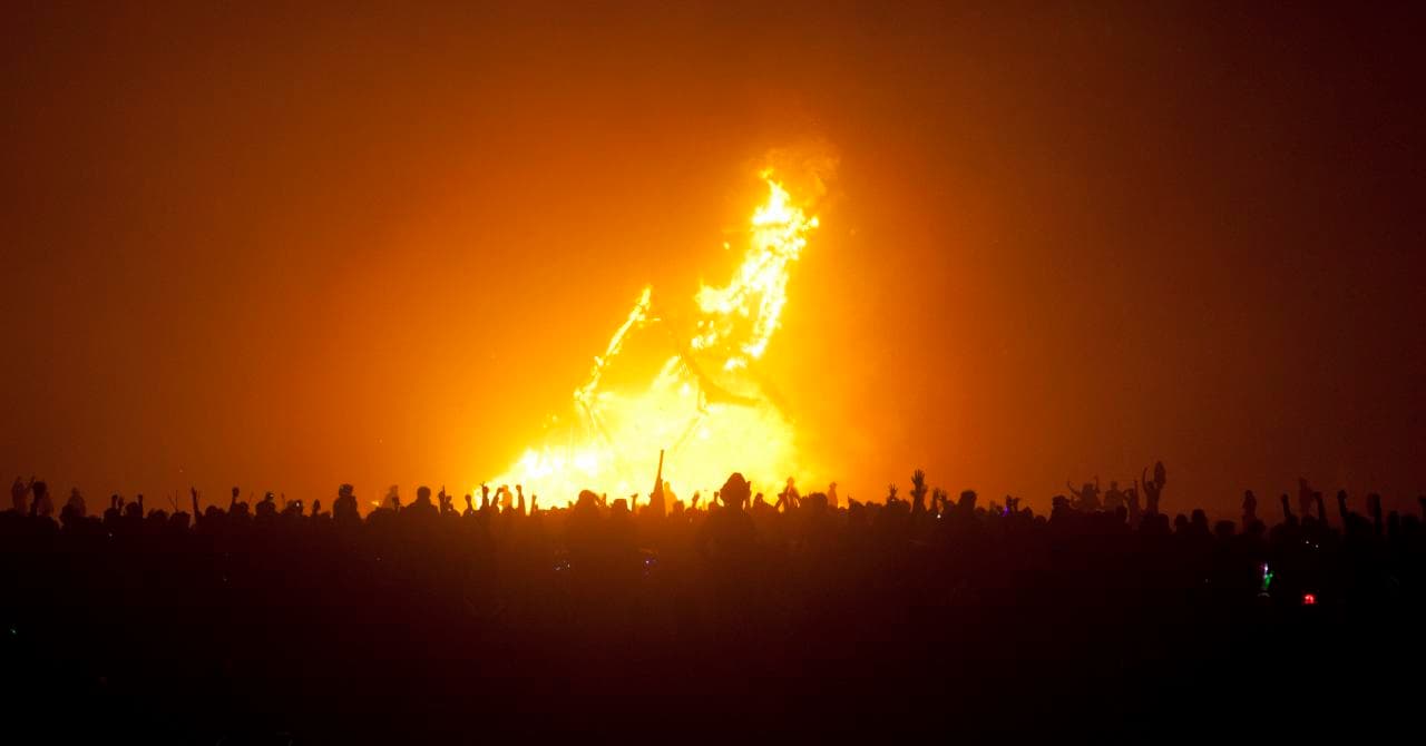 The Man effigy burning against the night sky as a silhouetted crowd raises their arms